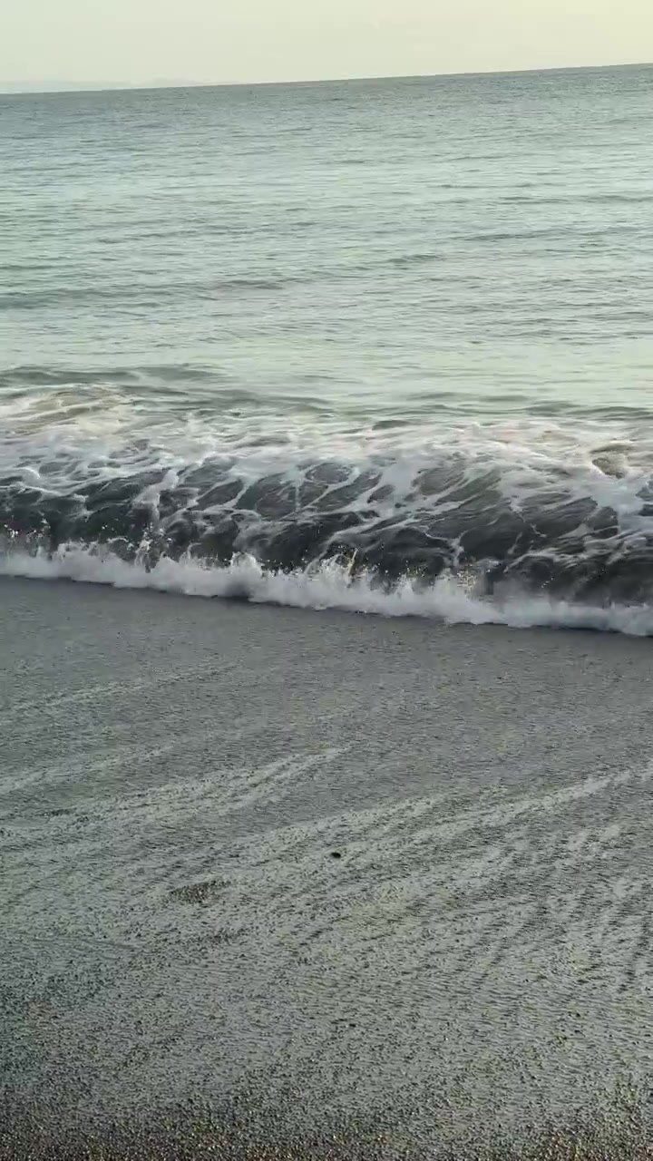 Onde oceaniche calme che si riversano su una spiaggia di sabbia scura.