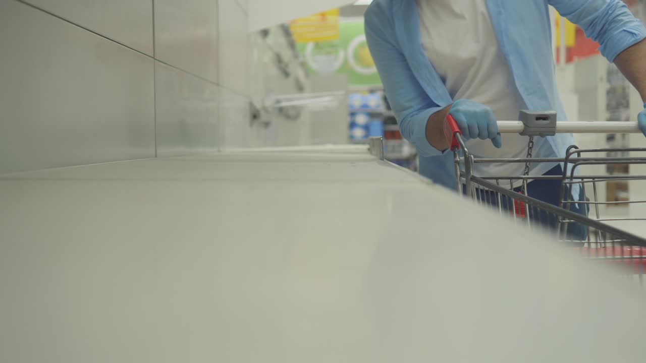 cliente masculino con un carrito de compras en el fondo de los estantes vacíos en la tienda