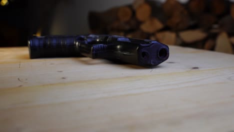 pistola de juguete negra yace plana sobre una mesa de madera y gira, con fondo oscuro