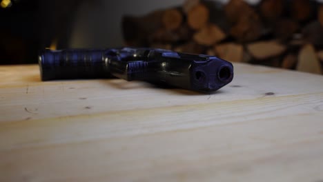 black toy gun lies flat on a wooden table and rotates, with dark background