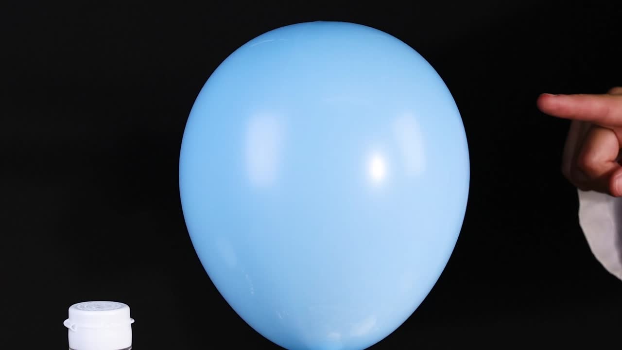 A blue balloon inflates on a bottle using powder, observed by a hand.