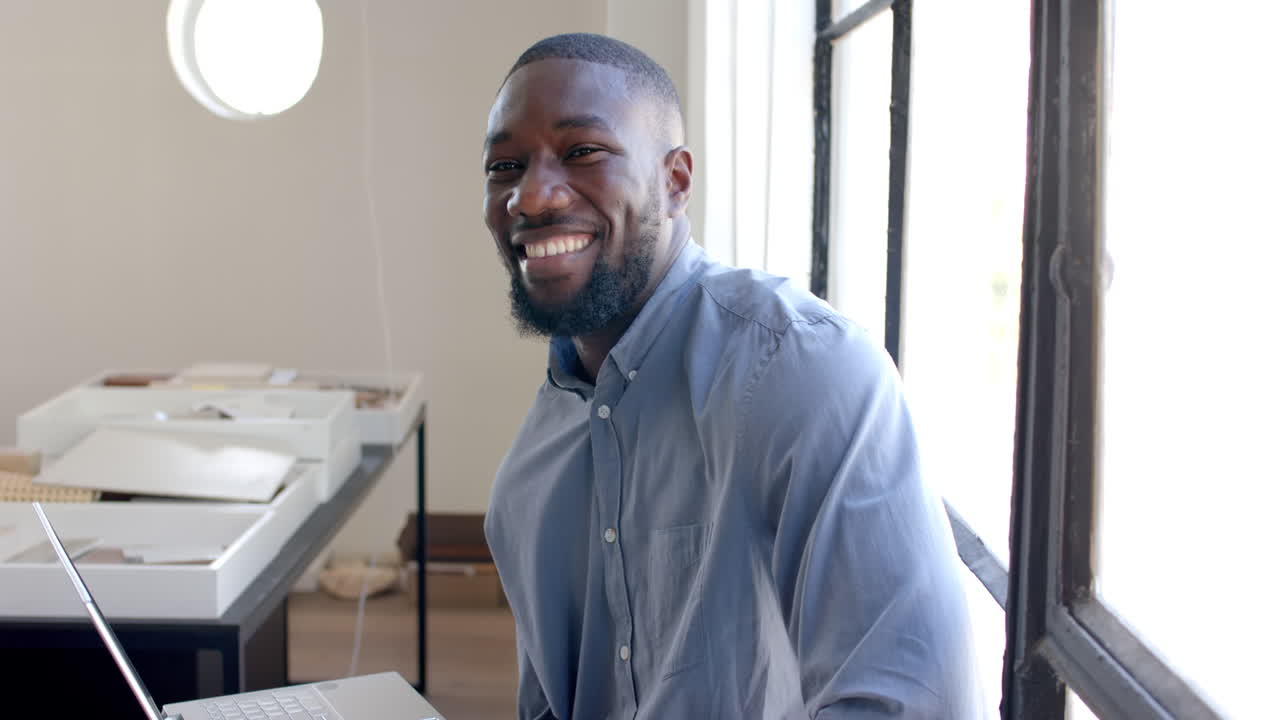 Smiling businessman sitting at desk, working on laptop in modern office