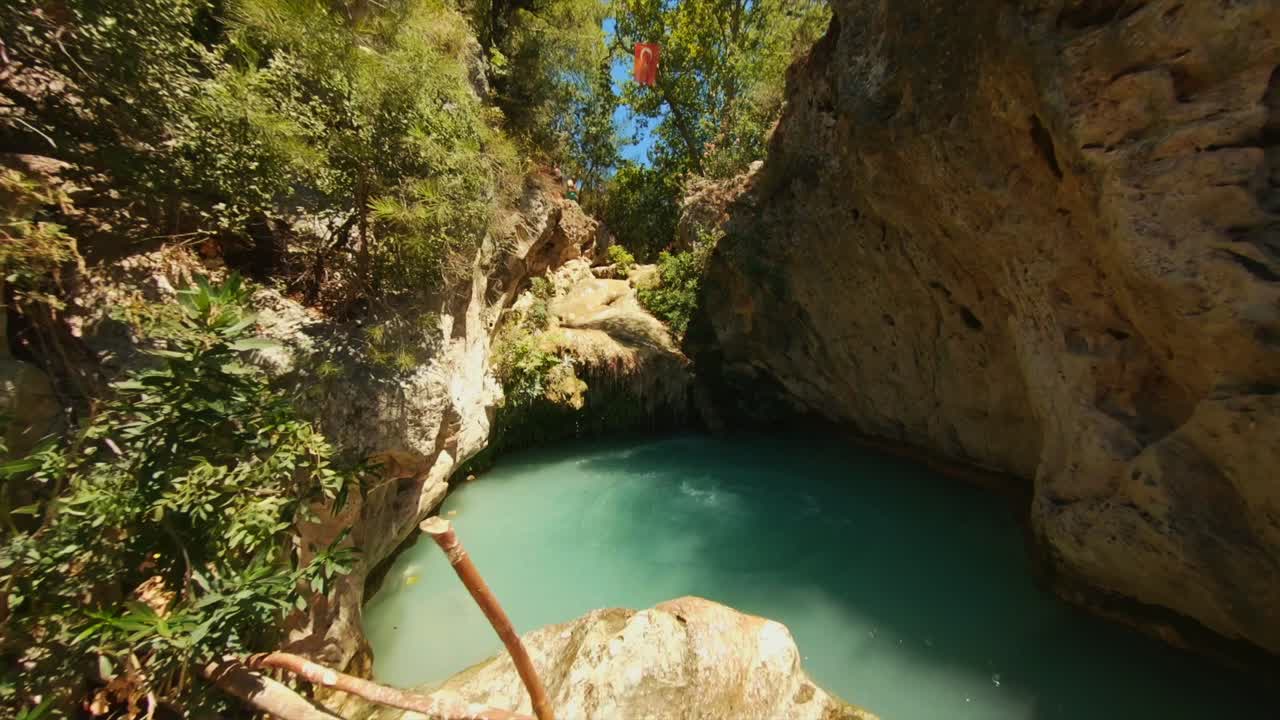mujer en bikini negro saltando a una fuente termal rodeada de rocas y árboles verdes