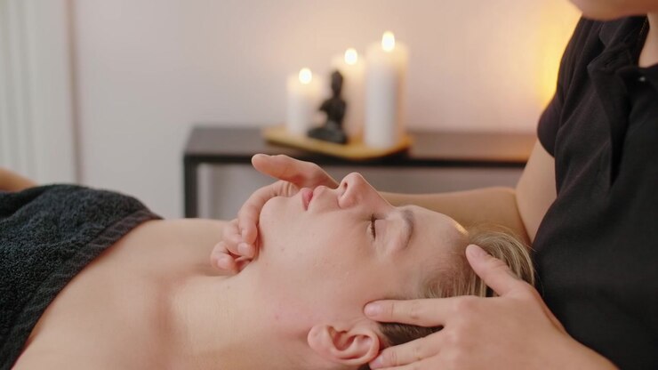 Professionel massageterapeut udfører ansigtsmassage på klient i spa.