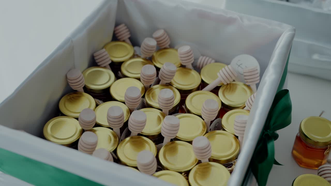 Box of small honey jars with gold lids and wooden dippers tied with a ribbon