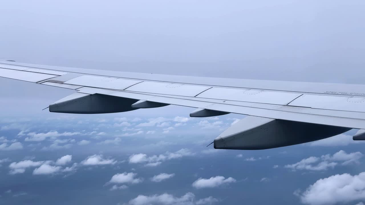 View from an airplane wing flying over clouds with a bright sky in the background