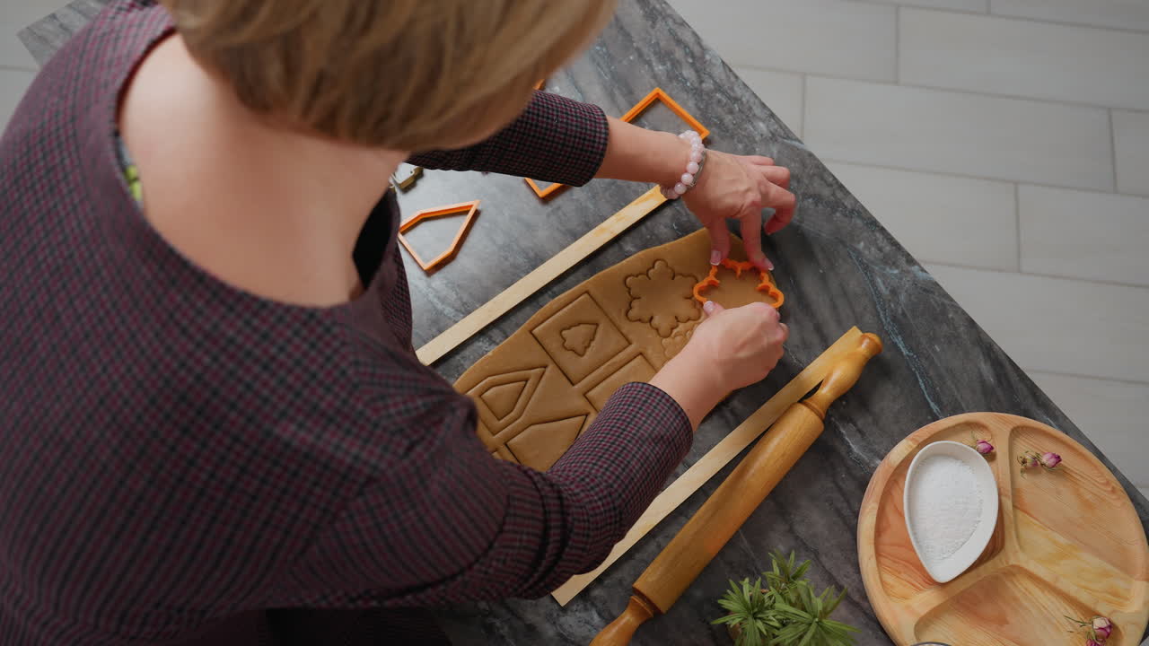 vista aérea de una mujer usando un cortador de naranja en la masa enrollada para crear formas precisas, herramientas de horneado, rodillo, y bandeja de madera con harina cerca estableció la escena para la preparación de pasteles caseros