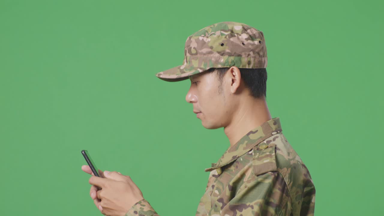 Primo piano di soldato asiatico di profilo che usa lo smartphone mentre cammina in studio con sfondo green screen