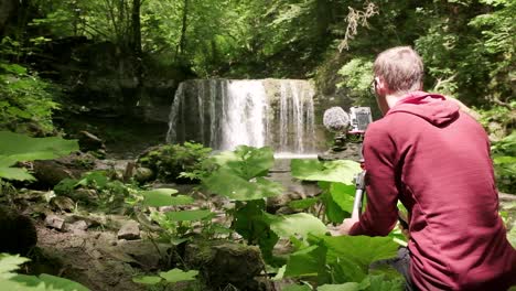 fotógrafo configurando su cámara y trípode para capturar una foto de larga exposición de la cascada en verano