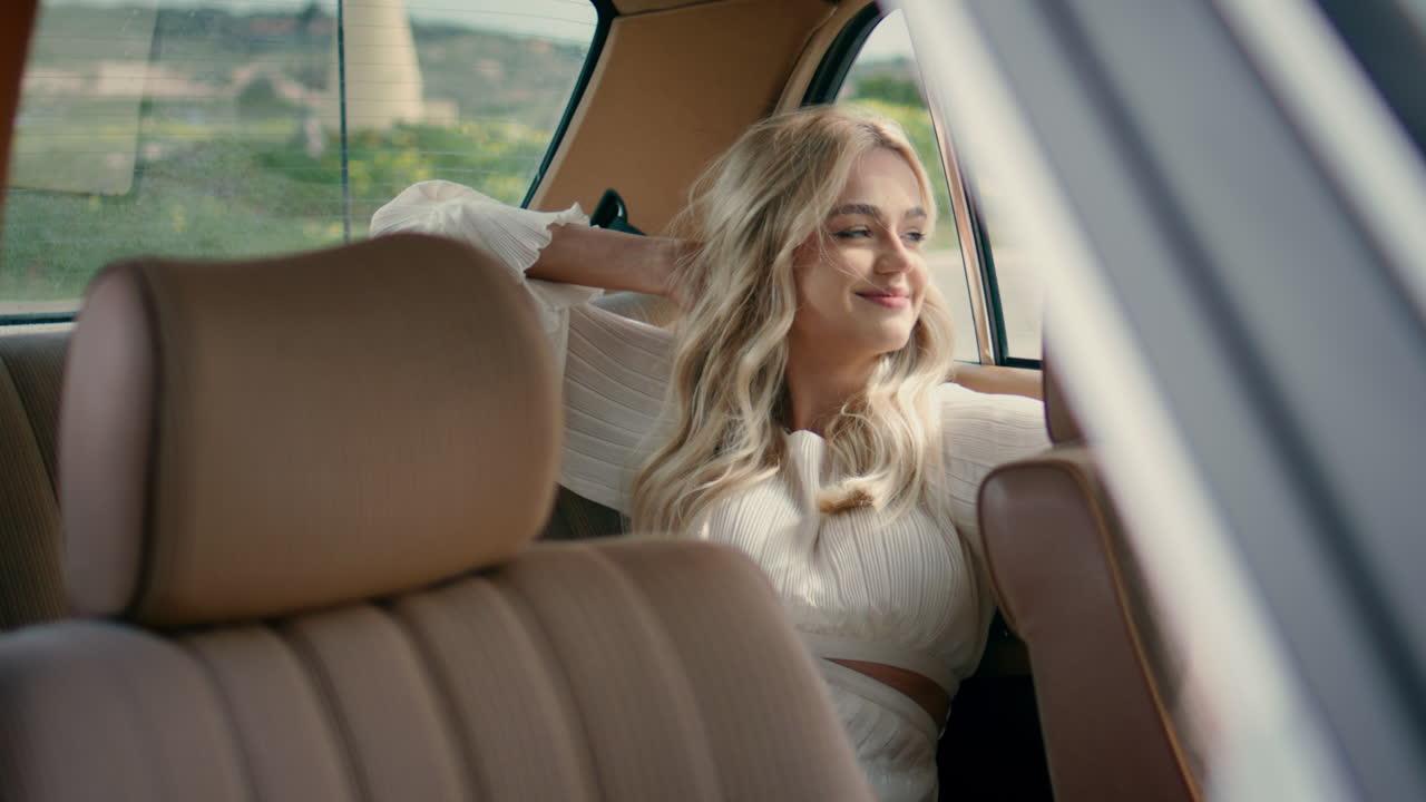 una mujer alegre sentada en el asiento trasero de un auto retro bajo la luz del sol de verano.
