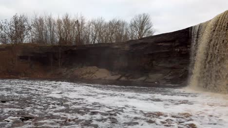 Estonia,-impressive-Jägala-Waterfall's-fallen-water-vapor-from-side-view-at-cloudy-and-early-wintery-day