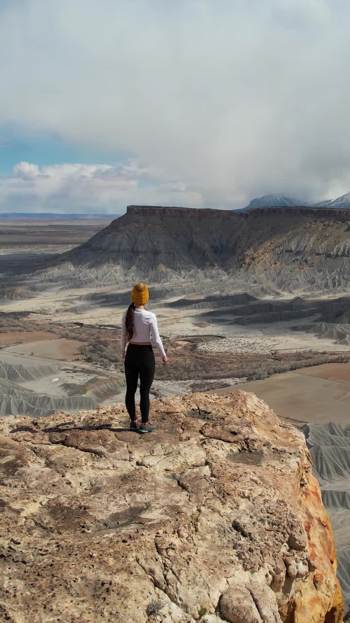 Woman overlooking a vast desert canyon landscape from a cliff edge