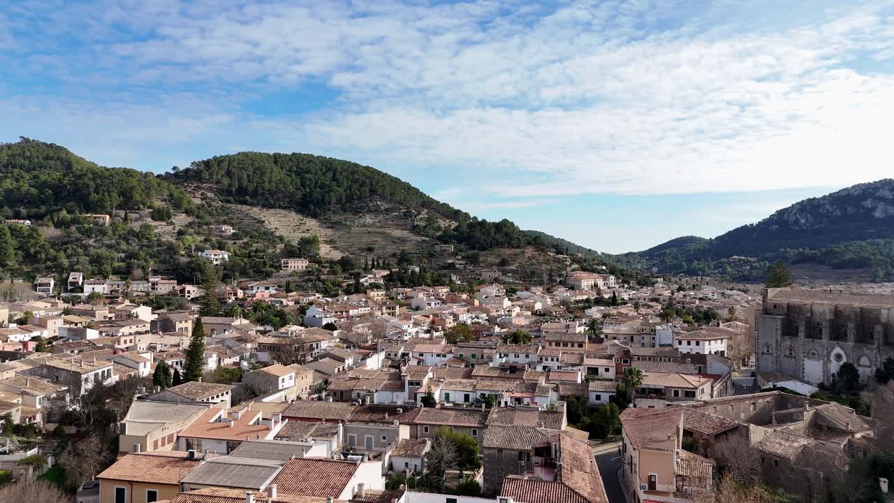 Ripresa aerea con drone in ascesa che mostra l'antica città di Esporles con montagne verdi sullo sfondo in estate - Maiorca, Spagna.