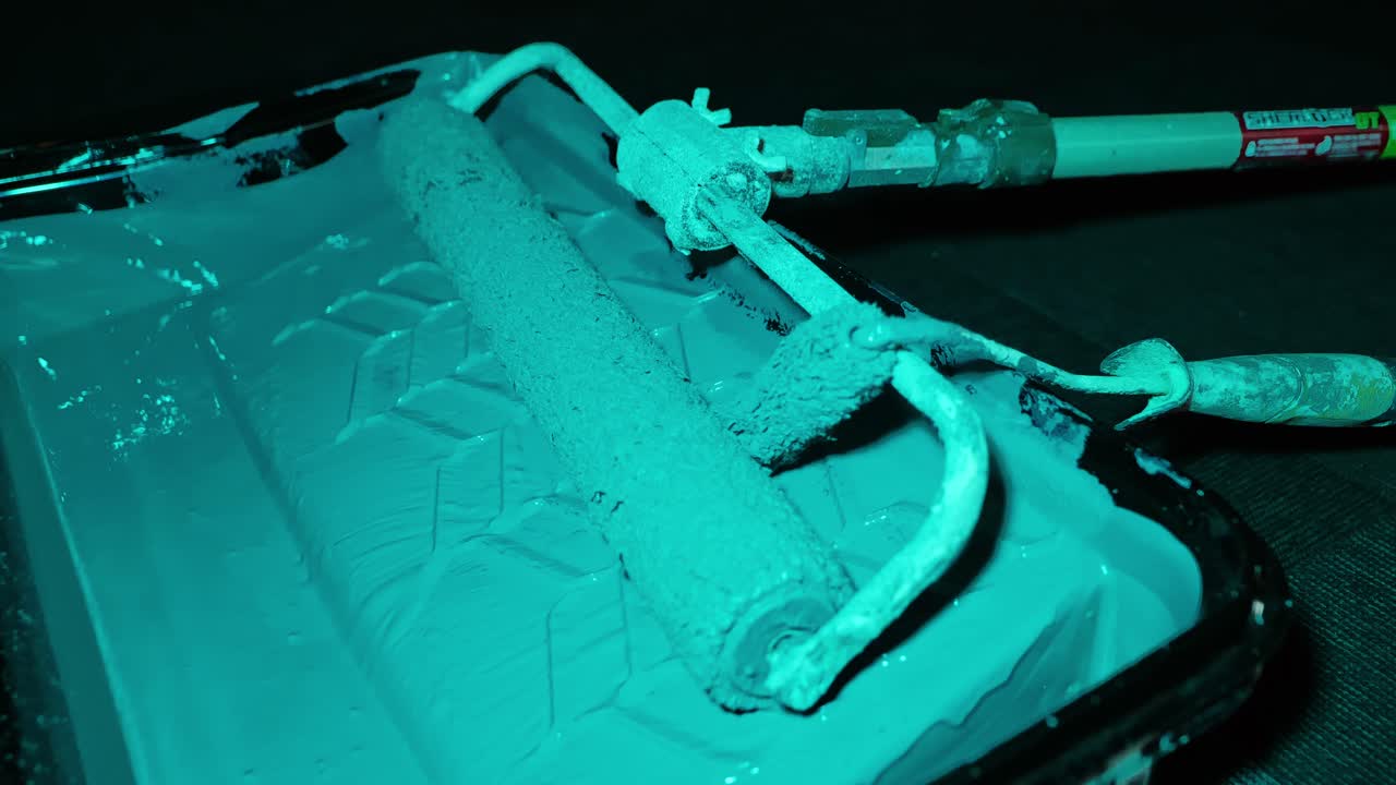 Teal lighting highlights gray roller in paint tray ready for interior wall work