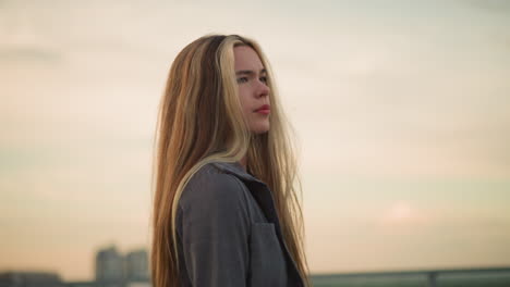 side view of lady in grey clothing touching her hair while walking along iron rail, looking tired and contemplative with a blurred background