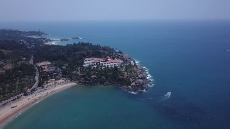 Raviz-Kovalam-En-Un-Acantilado-Costero-Con-Un-Barco-Que-Viaja-En-Aguas-Prístinas-Del-Océano-En-Kerala,-India---Drone-Aéreo