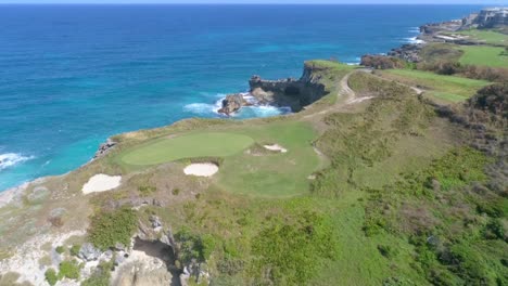 scenic view of rocky seashore landscape, green golf course greens above edge of cliffs and sandy pits by blue ocean water, macao, china, overhead aerial pull back