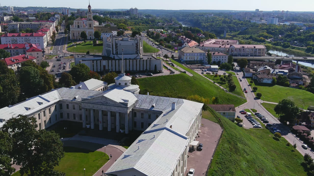 Letecký pohled dronem na centrum města Grodno s historickými budovami, silnicemi, zelenými kopci a městskou krajinou s řekou v dálce v Bělorusku.