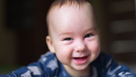 sweet toothless smile of a beautiful baby boy. little child lies on his belly holding head up and looking into camera. close up.