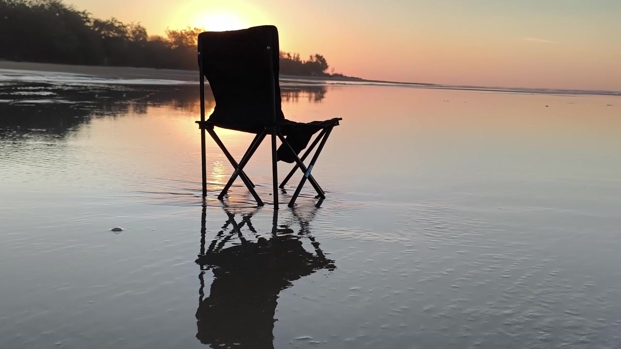 Leerer Klappstuhl am nassen Strand bei Sonnenuntergang.