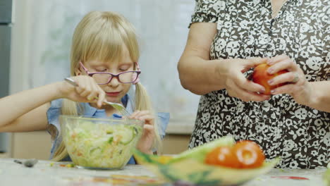 a funny girl eats a salad from a large bowl next to her grandmother 3