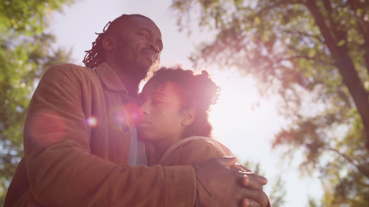 retrato de padre abrazando a su hija cerrando los ojos a la luz dorada del sol.
