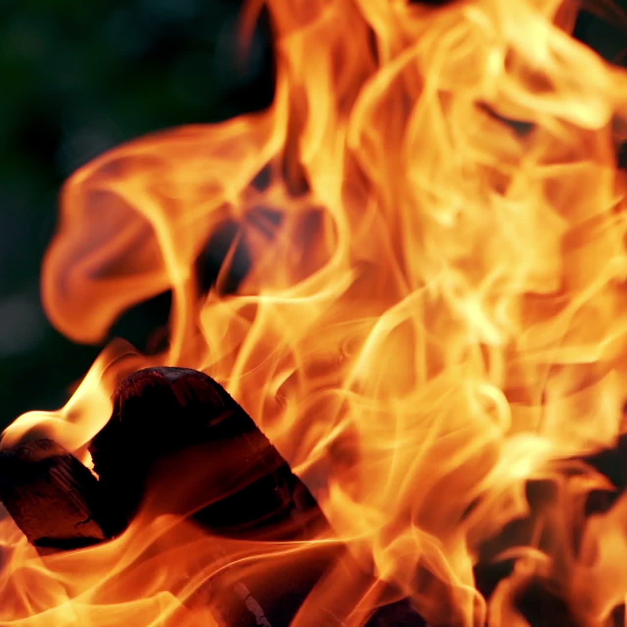 Orange flame on smoldered logs on blurred background. Bright campfire in the street in the evening in summer. Close-up.