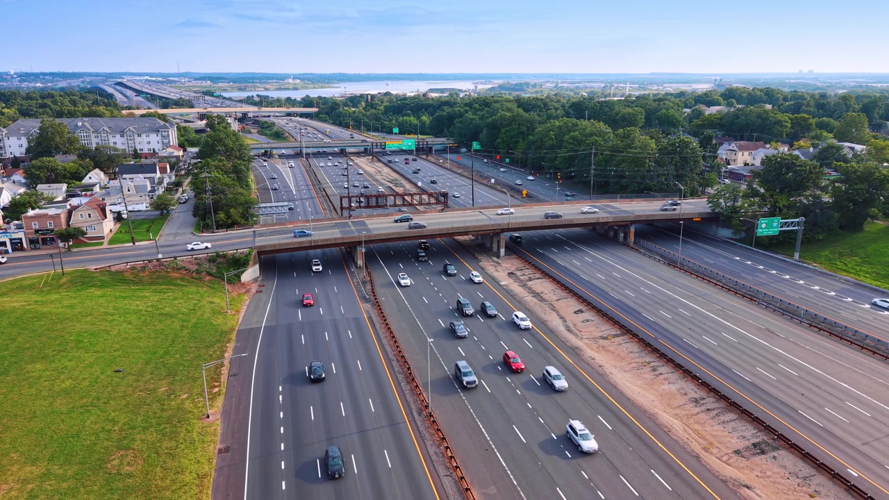 Afternoon sun over highway overpass near residential area, New Jersey. Wide aerial shot of green grass lawn, multi lane road and driving cars.