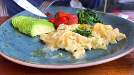 comiendo un desayuno mediterráneo saludable tradicional en españa, huevos revueltos con aguacate, tomate y espinacas, tiro de 4k