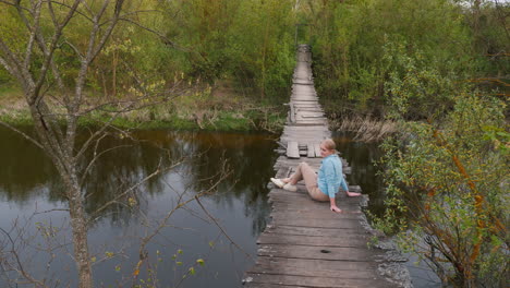 mujer sentada en un viejo puente de madera sobre un río en un bosque