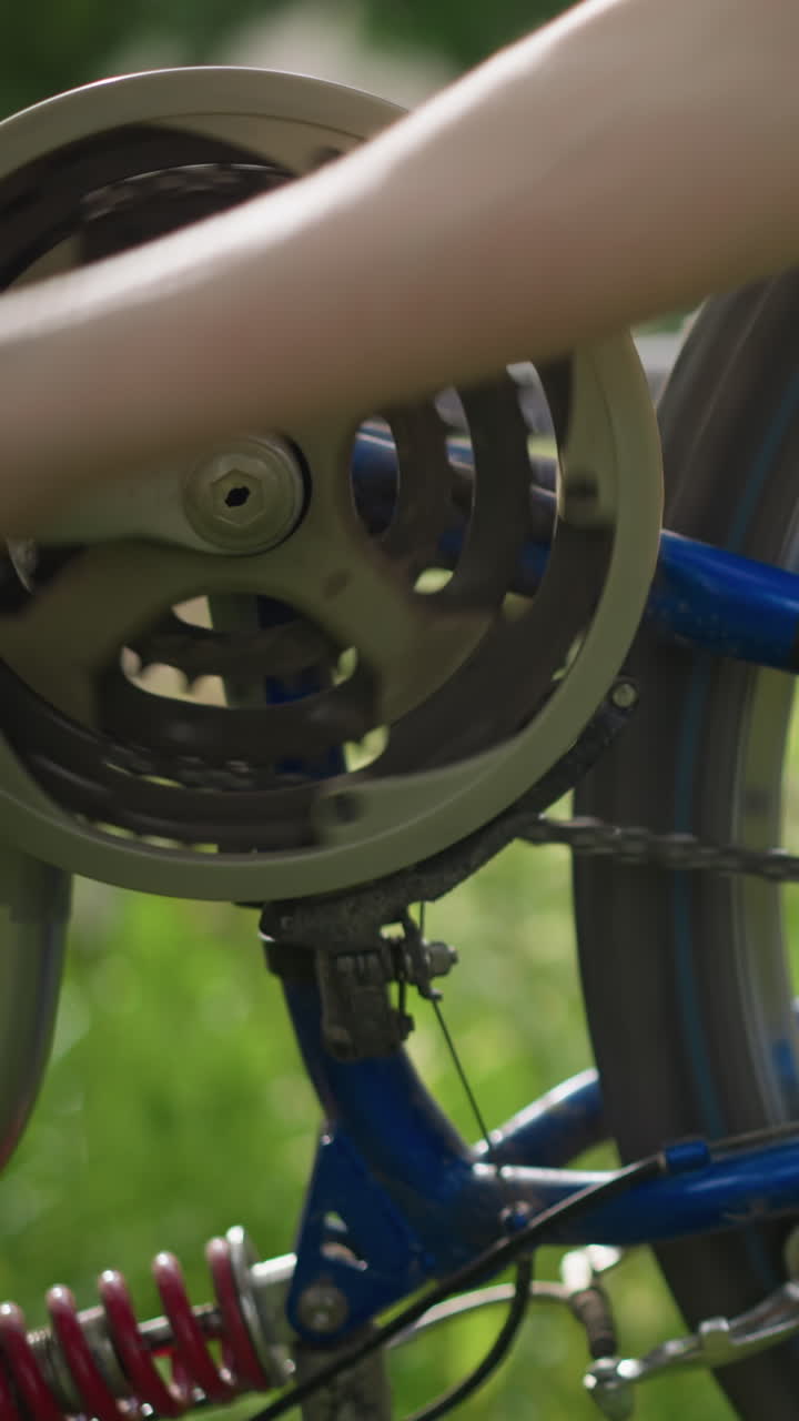 자전거의 바를 회전시키는 누군가의 손의 클로즈업 부분적인 시각, 체인과 기어 시스템에 초점을 맞추고, 배경에는 녹색의 부드럽게 흐릿한 시각이 있습니다.