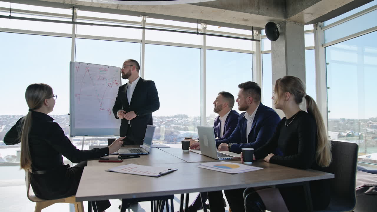 Emotional speech in front of team. Colleagues sitting at the table and listening to a man presenting chart. Business meeting in the office for coworkers.