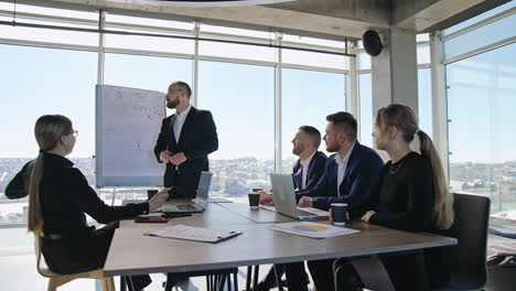 emotional speech in front of team. colleagues sitting at the table and listening to a man presenting chart. business meeting in the office for coworkers.