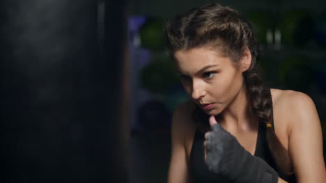 close up view of a young woman punching a boxing bag with her hands wrapped in boxing tapes. boxing in slow motion