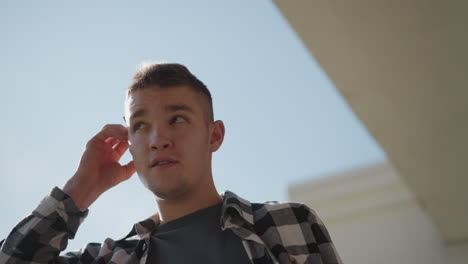 portrait view of young man in black white plaid shirt descending metal staircase against clear sky removes cigarette from ear raises hand flicks lighter sparks tip prepares inhale smoke