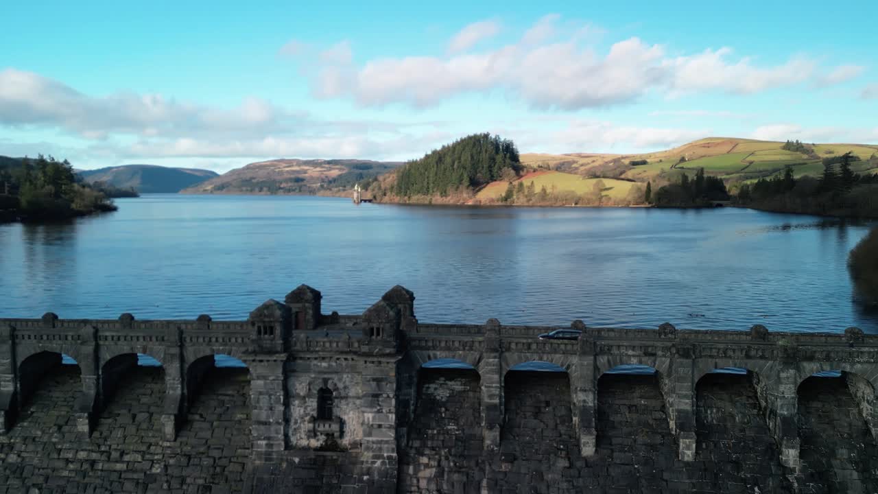 Drone close in clockwise rotate of Lake Vyrnwy dam ramparts on a crisp sunny winter afternoon, cars crossing - Wales, UK