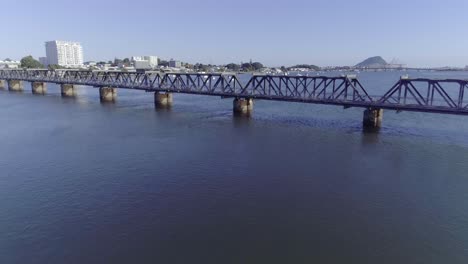 Fliegen-In-Richtung-Matapihi-Eisenbahnbrücke-Mit-Der-Stadt-Tauranga-Im-Hintergrund,-Bay-Of-Plenty,-Antenne