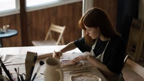 a red-haired potter girl cuts a circle from a piece of clay using special tools