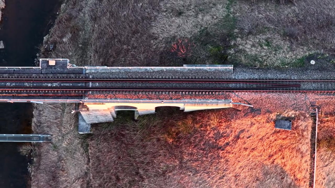 Scenic railway bridge crossing a river at sunset in aerial top down view