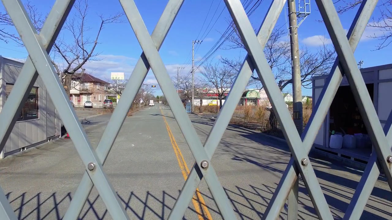 Portão de metal se abre para revelar uma rua deserta em Fukushima