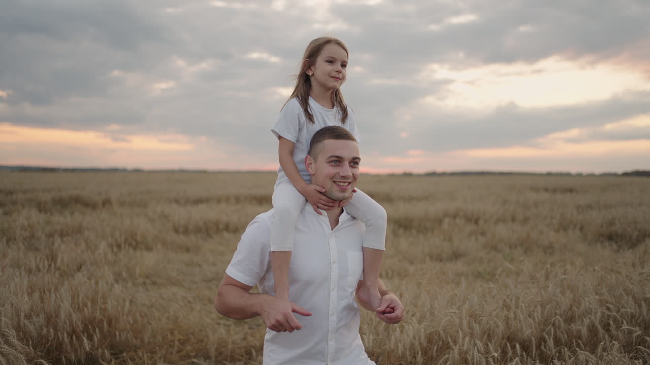bambino felice e padre stanno giocando nel campo di grano maturo. figlia piccola sulle spalle dei padri. bambino ragazzo e padre viaggiano sul campo. bambino e genitore giocano in natura. famiglia felice e concetto di infanzia
