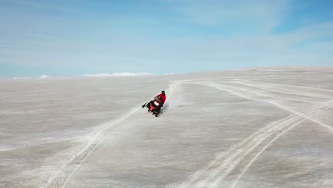Aerial-view-of-a-person-doing-stunts-on-a-snowmobile,-on-the-surface-of-a-glacier-in-Iceland,-on-a-sunny-day