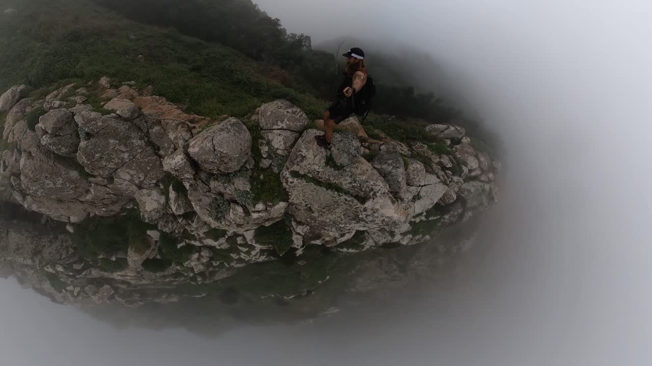 A young and fit solo hiker is jumping between rocks on the edge of the steep cliff of Espigao Amorelo in Madeira, surrounded by mist, fog and clouds. A risky and dangerous act full of adrenaline.