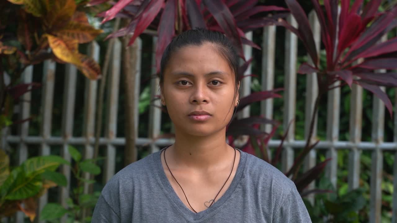 필리핀에 있는 고아원의 배경에 아름다운 식물이 있는 카메라를 바라보는 필리핀 고아 소녀의 모습을 클로즈업 - 정적 샷