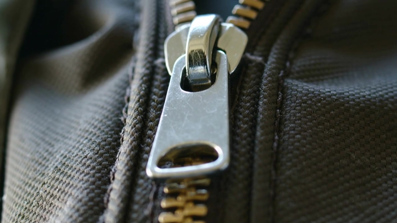 Cursor prateado de zíper subindo na mochila, abrindo os dentes de latão e revelando o forro, após ser puxado.