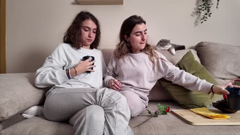 two women relaxing on couch with cat