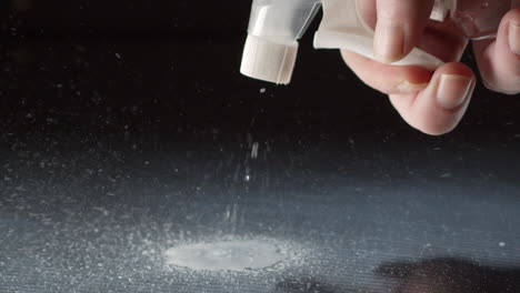 spray bottle being squeezed on black stainless steel surface - detail slow-motion close up shot