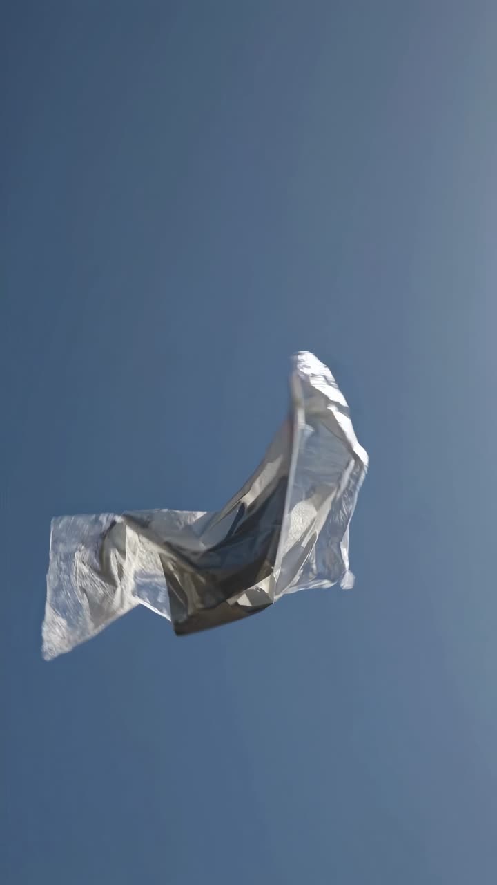 A low-angle shot of a crumpled metallic object floating against a clear blue sky