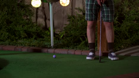 Eine-Nahaufnahme-Eines-Violetten-Minigolfballs,-Der-Mit-Einem-Schläger-Getroffen-Wird.-Der-Schlag-Ist-Schrecklich-Und-Der-Ball-Rollt-Zurück-Zum-Golfspieler