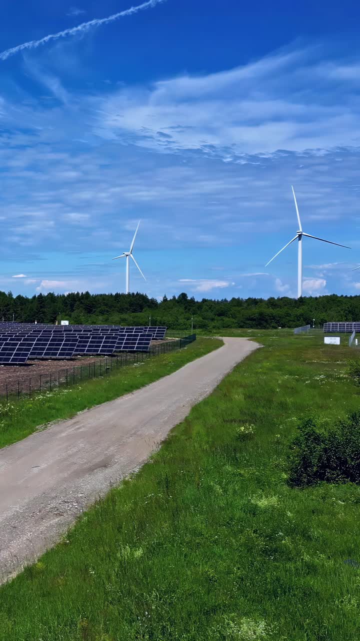 Aerial rising shot reveals a solar farm and modern wind turbines in the lush Latvian countryside, showcasing clean renewable energy and rural development
